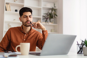 Arab man using laptop sitting at desk in office, a Photo by Prostock-Studio