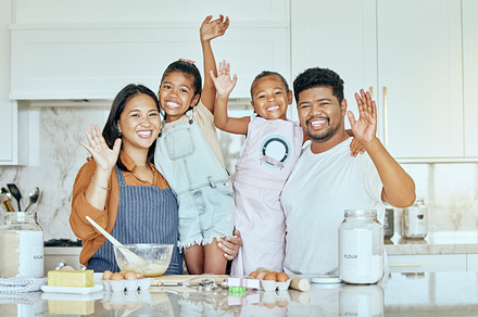 Family, love and baking together in kitchen with smile, happy and wave with ingredients on counter or table. Portrait of girl kids, mother and father enjoy cooking or bake while bonding in home, a Photo by Peopleimages.com