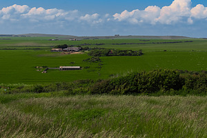 Rural farm buildings surrounded by vast green fields under a blu, a Photo by Studio ANNA