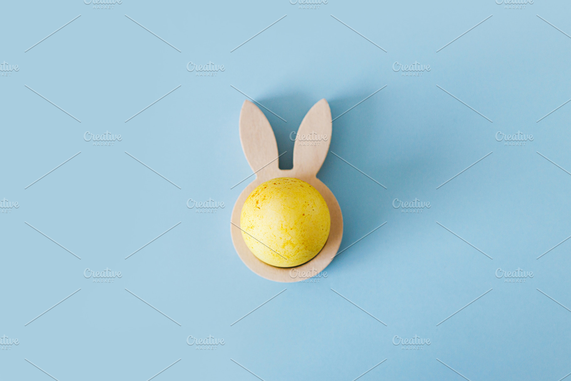 Happy Easter! Modern yellow easter egg in wooden bunny ears hold, a Holiday Photo by Sonjachni