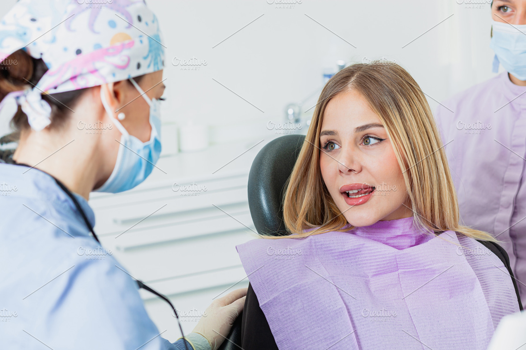 Dentist wearing surgical mask listening to young woman in dental clinic, a Health & Medical Photo by Antonio Gravante Market
