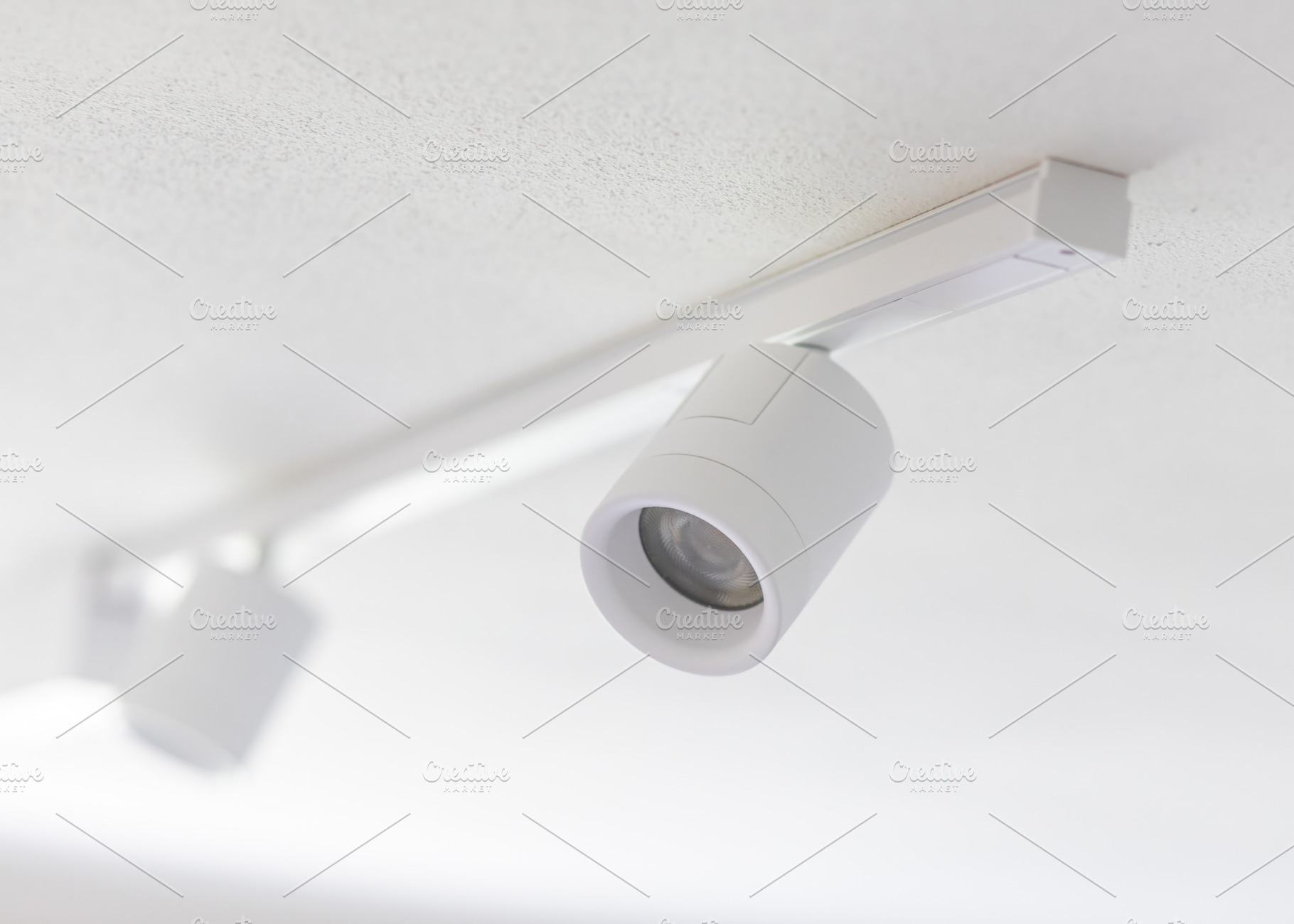 White spotlights hanging from ceiling track lighting system illuminating space, an Architecture Photo by Antonio Gravante Market