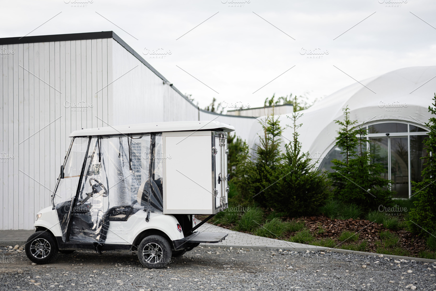 White utility golf cart parked near modern building and landscaped greenery, a Photo by AS photostudio