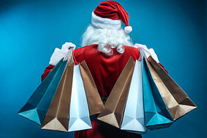 Santa Claus's backside carrying shopping bags and isolated blue, a Holiday Photo by Davizro's Market