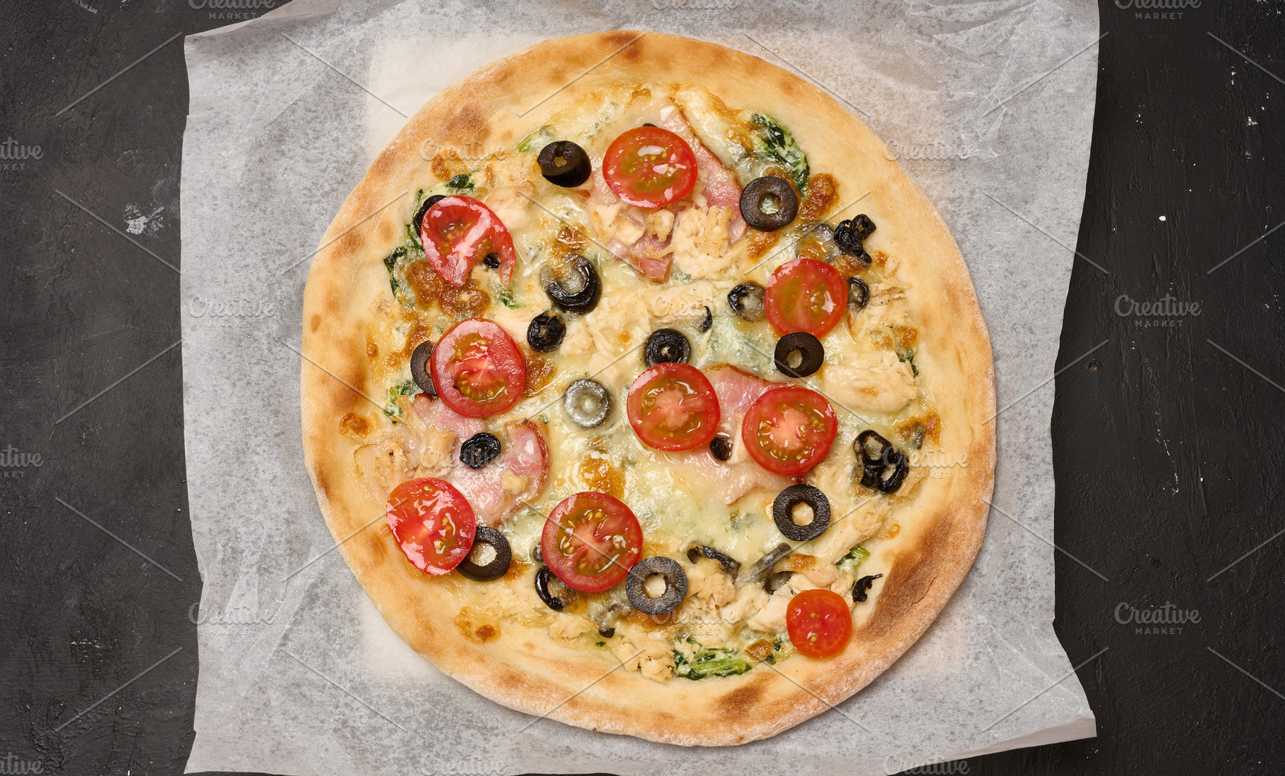 Round pizza with bacon, chicken, olives and cheese on parchment, a Food & Drink Photo by ndanko