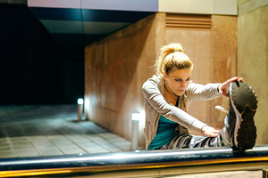 Woman runner stretching her legs before training at night on tow, a Sports & Recreation Photo by davidpereiras