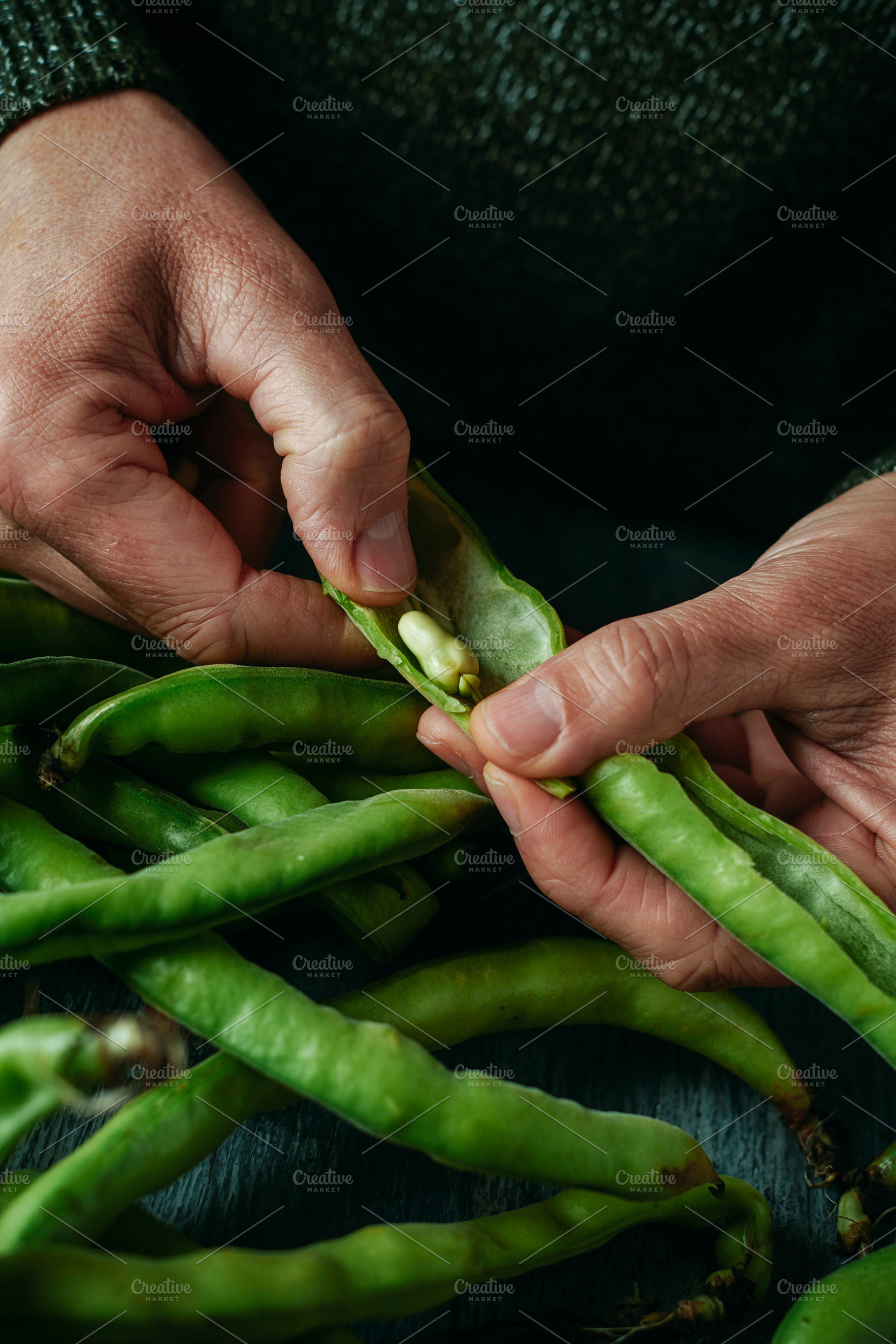 a man takes some broad beans out of its pod, a Photo by Nito