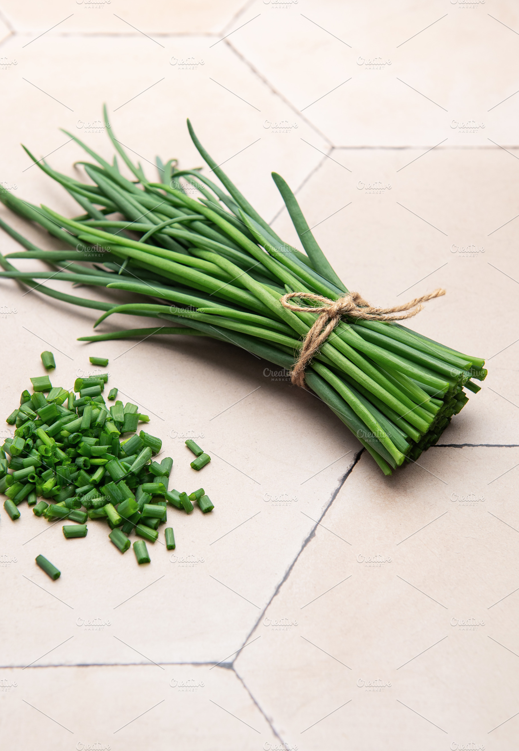 Freshly cut chives tied with twine on a tiled surface, a Food & Drink Photo by Olena Rudo