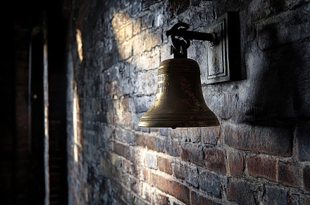 Bell mounted on dark brick wall cast, a Photo by Iftikhar Alam