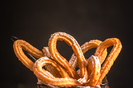 Traditional Spanish churros with sugar powder on the table. Dark and moody phot, a Food & Drink Photo by zakiroff