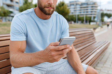 Young man sitting on a bench using smartphone in a modern urban park setting, a Technology Photo by AlyaAnd