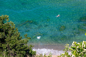A person swims in transparent turquoise water near a sandy shoreline, surrounde, a Holiday Photo by Ales Munt