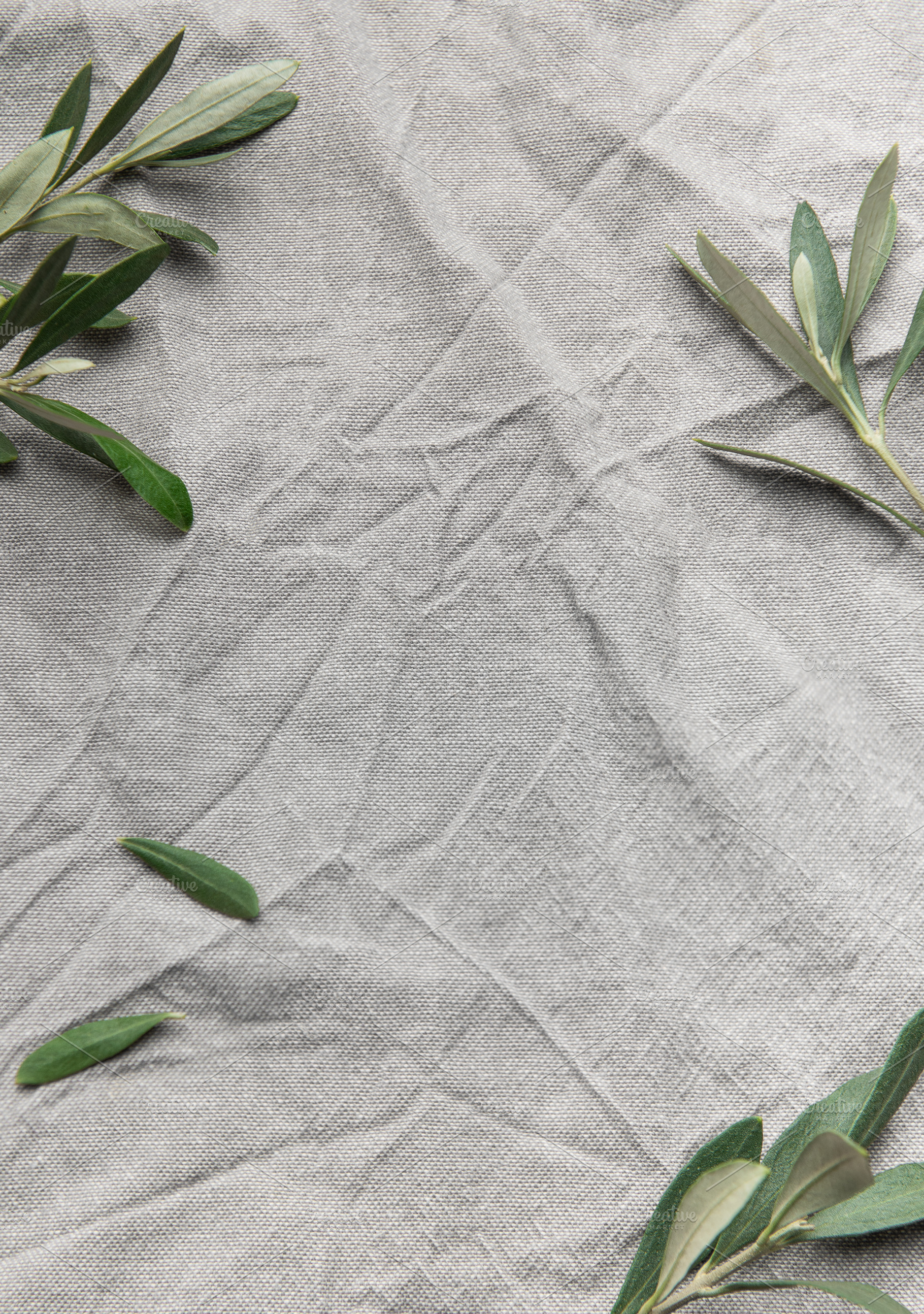 Olive branches framing wrinkled gray linen cloth background, a Background Photo by Olena Rudo