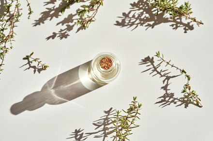 A bottle of thyme essential oil with fresh thyme on white backgr