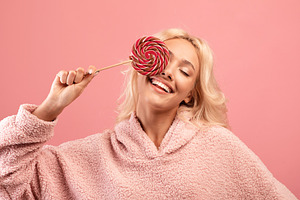 Joyful young woman holding candy on stick, covering one eye with lollipop and s, a Photo by Prostock-Studio