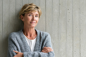 Middle-aged woman with a subtle smile, posing against a textured gray wall, a Person Photo by AlyaAnd
