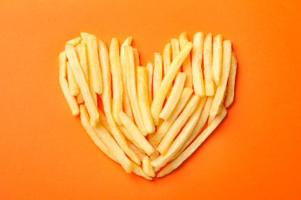 Handmade heart with tasty french fries on orange background, top