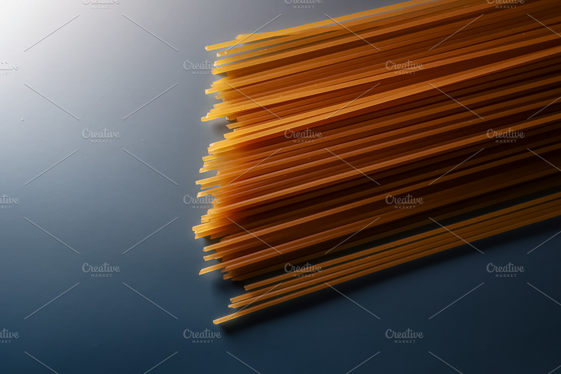 Uncooked whole wheat spaghetti noodles on a blue surface, prepar, a Photo by Studio ANNA