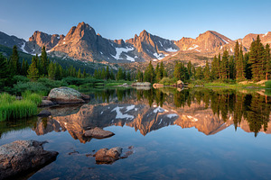 Mountain lake with reflections of lush greenery and rugged peaks at sunrise, a Nature Photo by AlyaAnd
