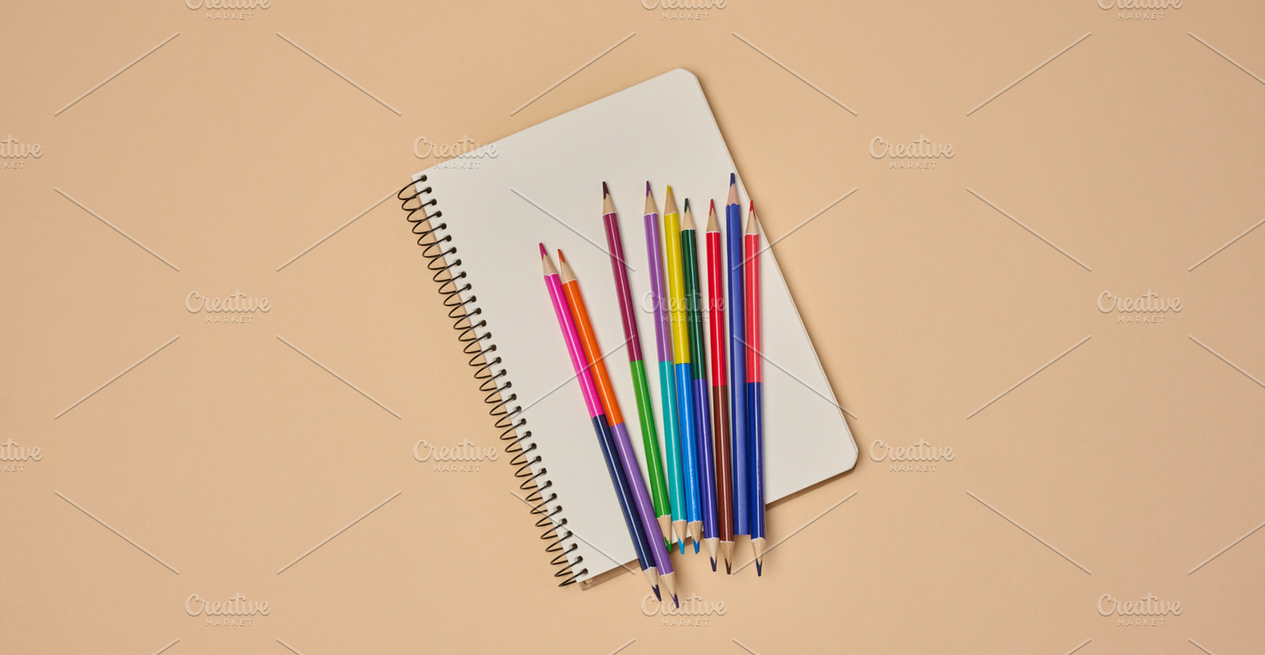 Top view of an open notebook with pastel-colored pencils on a be, a School & Education Photo by ndanko