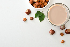 Glass of hazelnut drink on white table with nuts around, a Food & Drink Photo by Davizro's Market