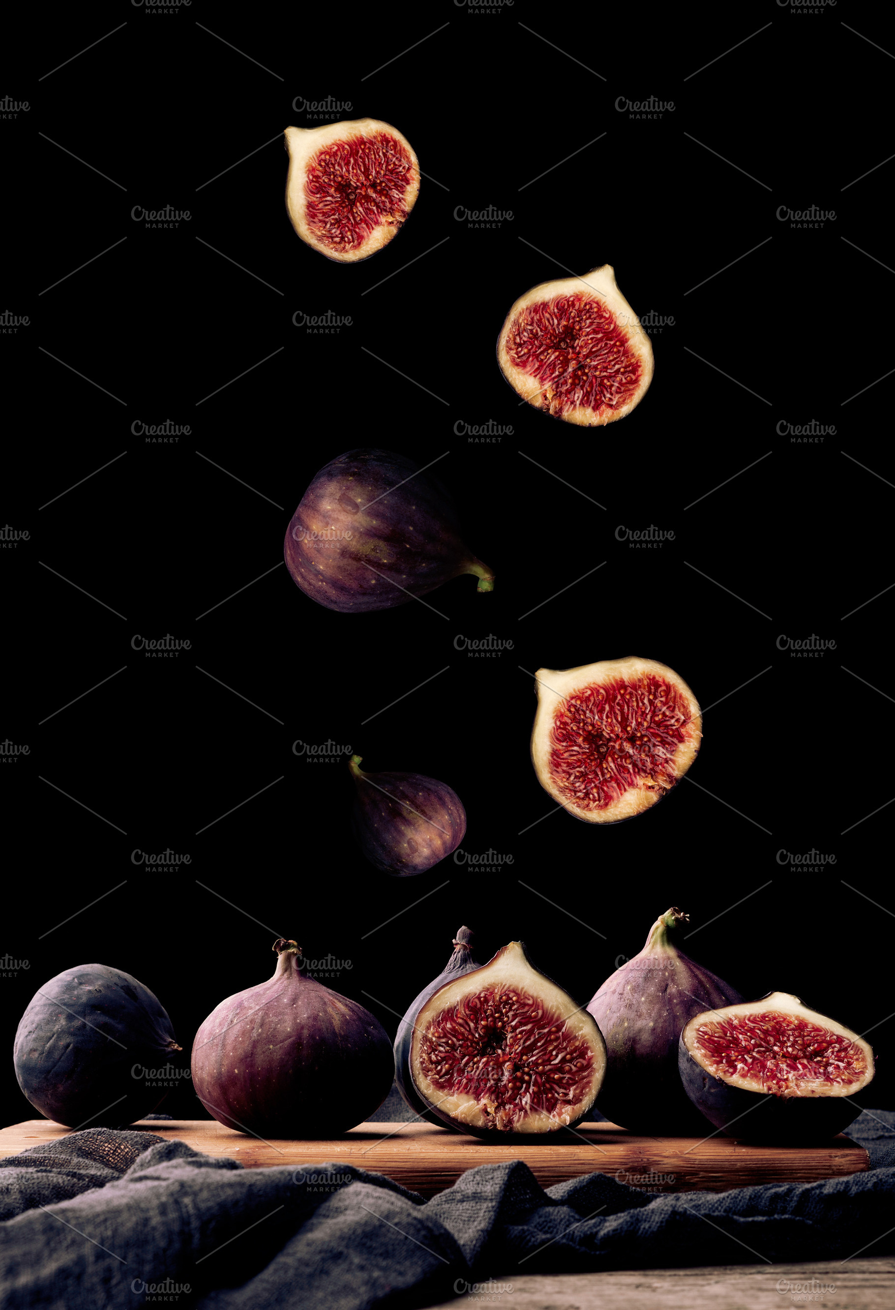 Ripe whole and sliced figs flying over a wooden board on a black, a Food & Drink Photo by ndanko