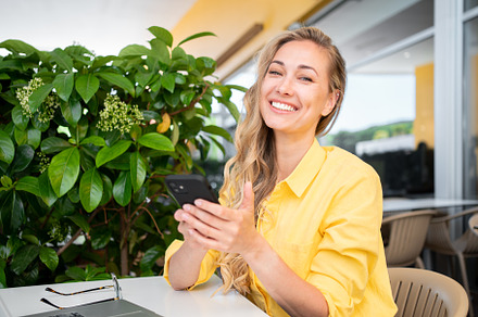 Happy freelancer woman holding smartphone at restaurant table, a Person Photo by andreonegin market
