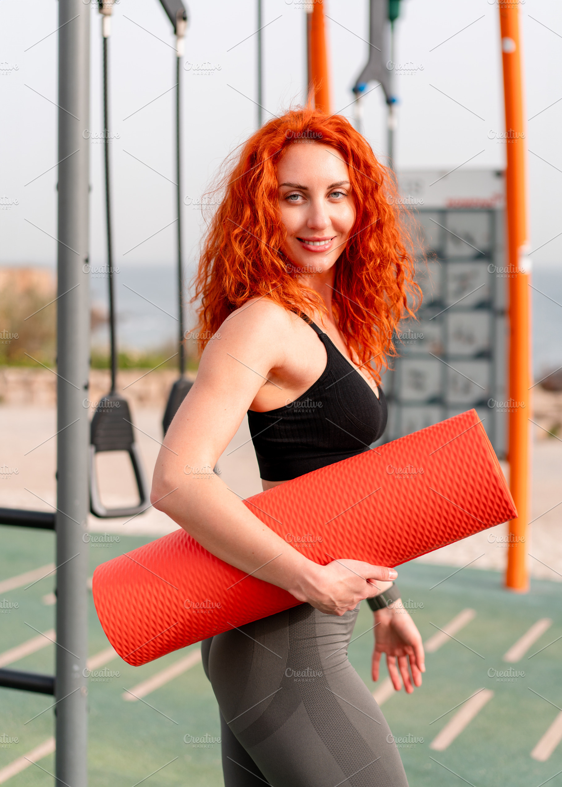 Smiling confident jogger woman holding rolled up mat at outdoor gym, a Person Photo by andreonegin market