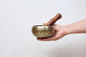 A person holding a metal singing bowl with a wooden stick in the