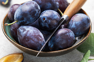 Fresh plums in bowl with knife on gray background, a Food & Drink Photo by Olena Rudo