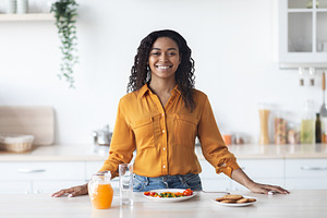 Cheerful black woman having proper breakfast, kitchen interior