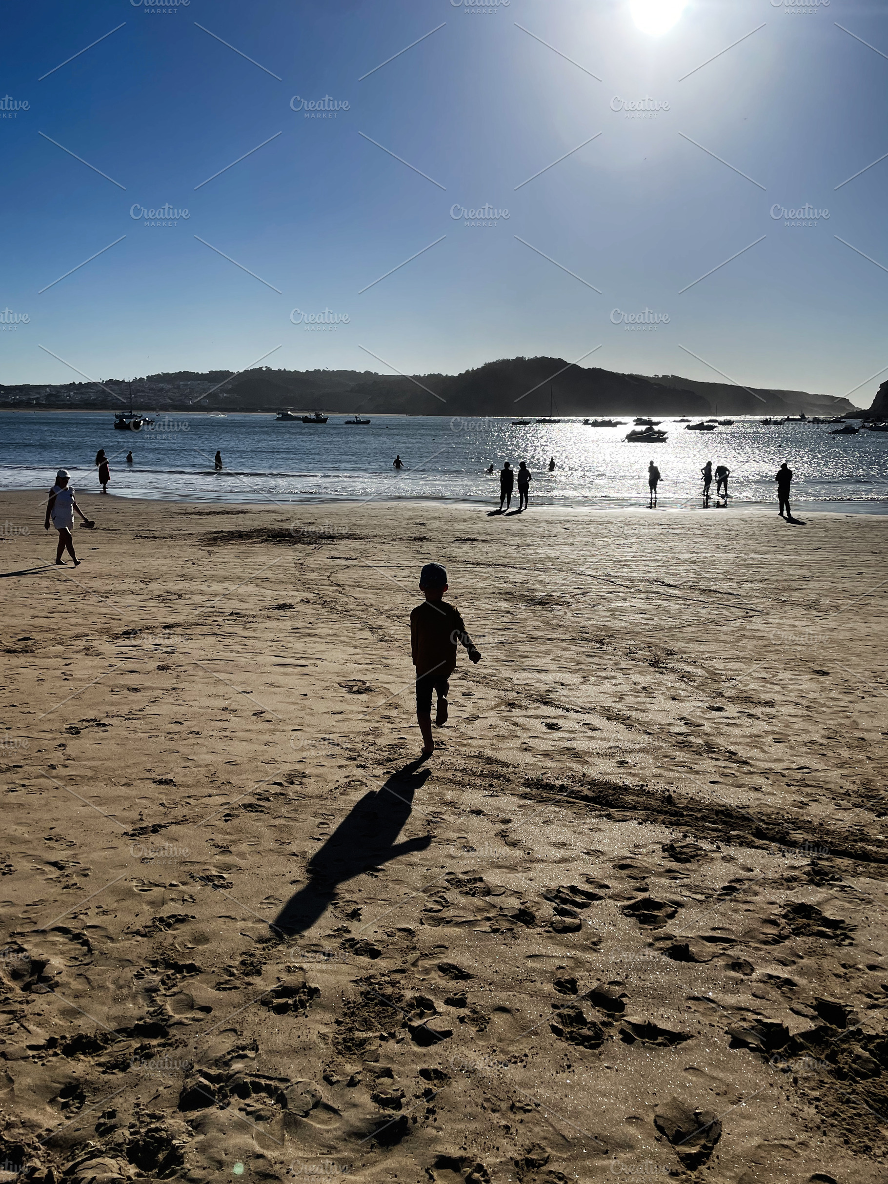 Silhouetted figures walk along a sunny beach by the calm water, a Photo by AS photostudio