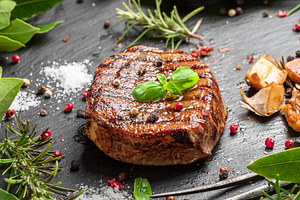 Grilled delicious ribeye steak and some seasonings and herbs on, a Food & Drink Photo by Volff