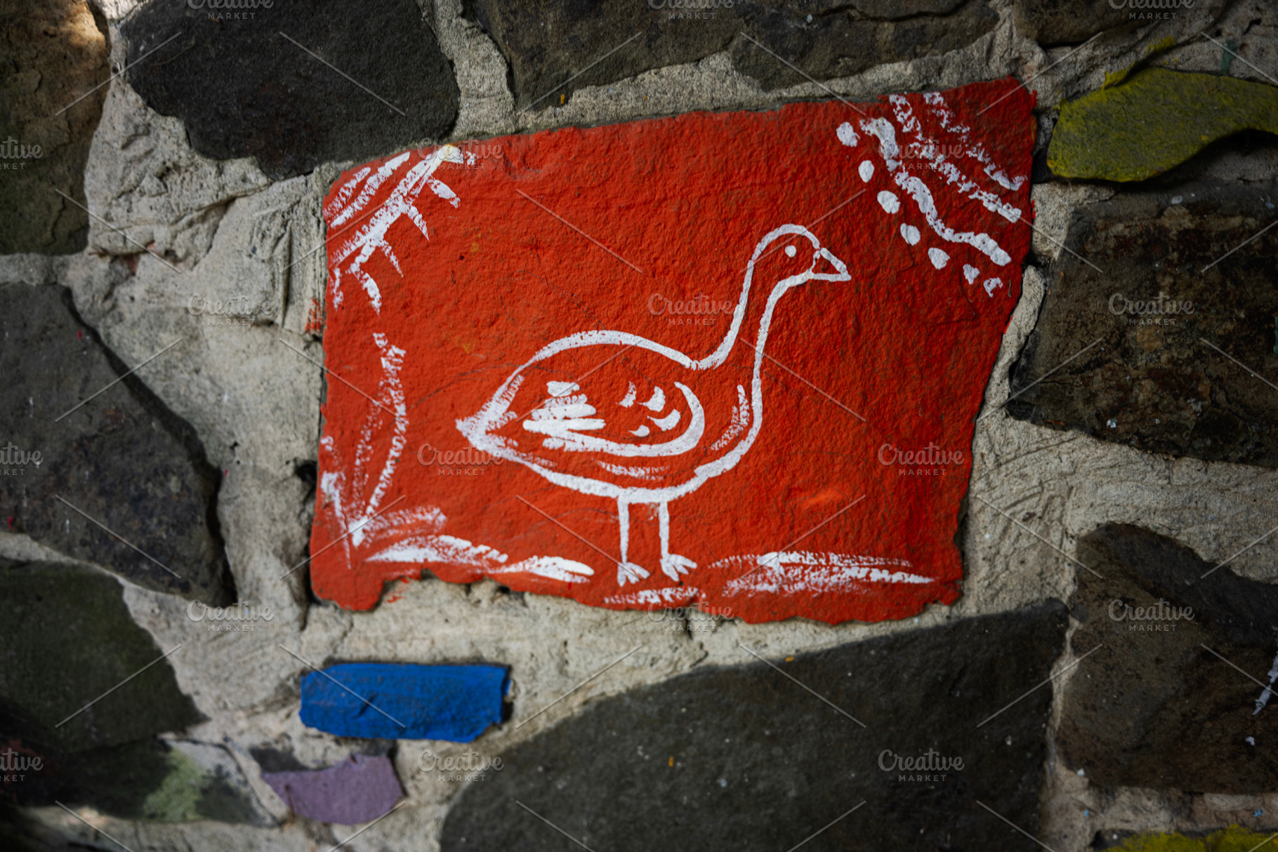 Hand-painted red stone art depicting a bird against a textured wall, a Photo by AS photostudio