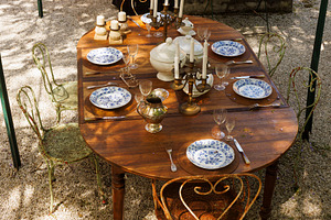 Wooden outdoor table in a garden courtyard set with vintage plat, a Food & Drink Photo by Bepslabor
