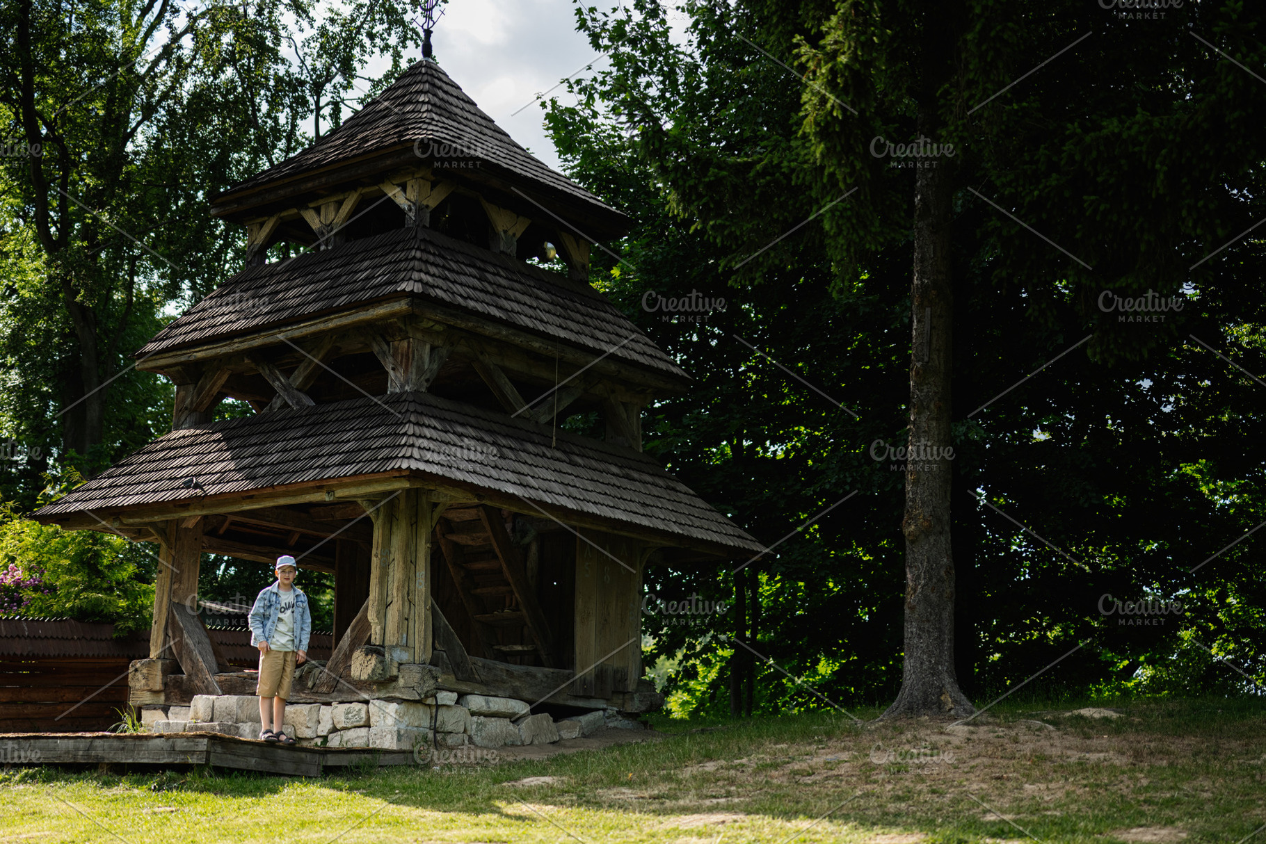 Wooden bell tower surrounded by trees with a person nearby in daylight, a Person Photo by AS photostudio