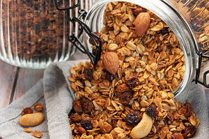 Granola mix with oats, nuts, and dried fruits spilling onto a gr, a Food & Drink Photo by Olena Rudo