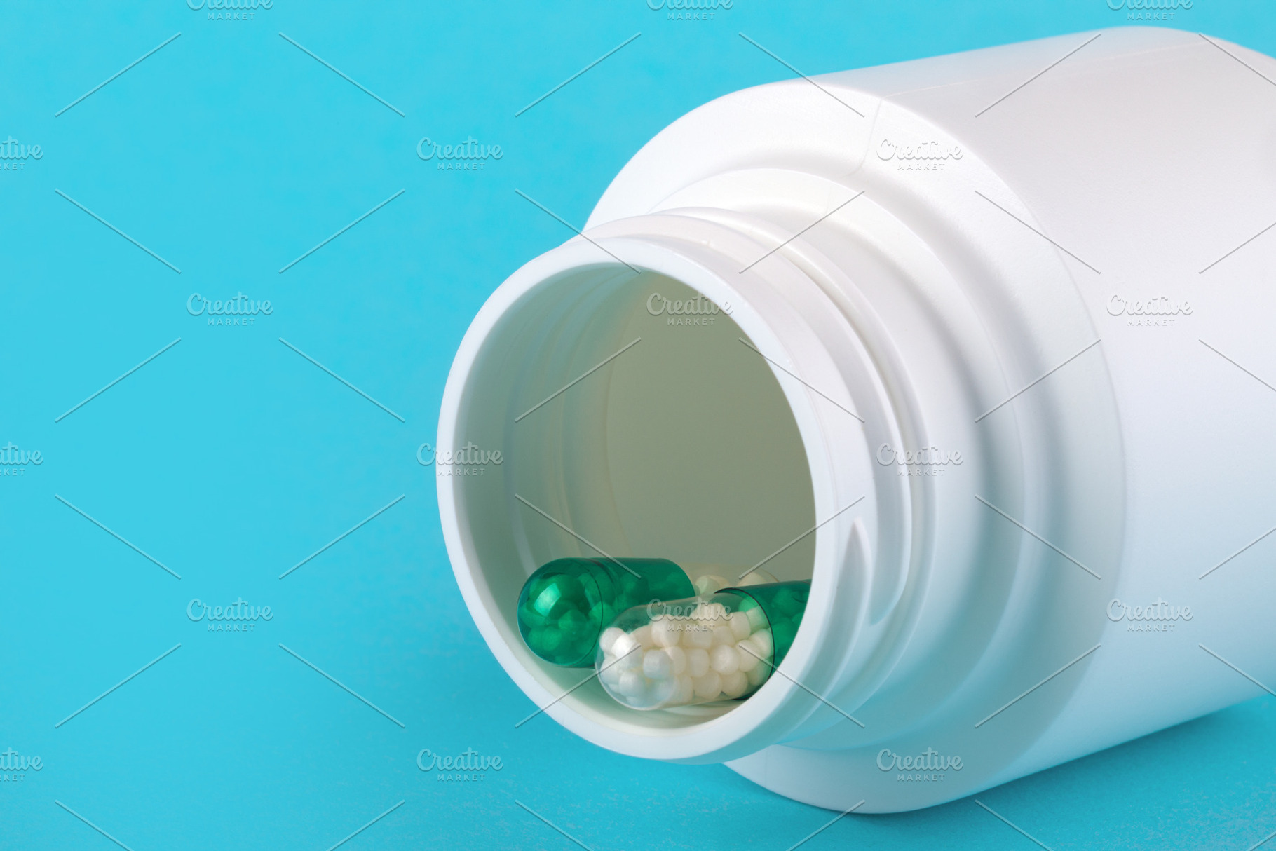 Close-up of green capsule and white pills in a white medicine bottle on a blue, a Health & Medical Photo by Ales Munt