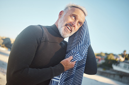 Surfer, towel and swimming with senior man drying hair after a swim, surf and water sports while on a surfing trip, adventure and summer vacation. Happy male smiling in a wetsuit while on holiday, a Photo by Peopleimages.com