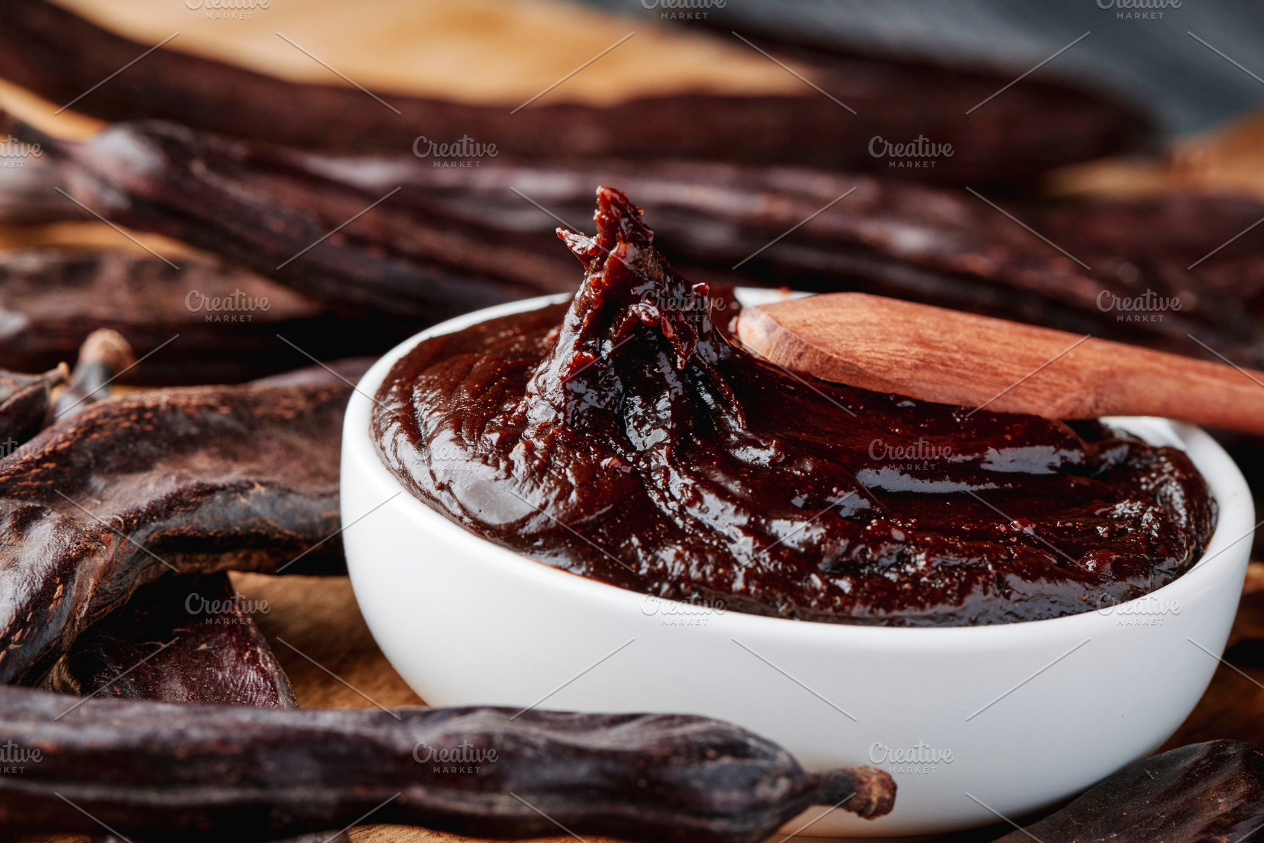 a wooden spoon stirs thick carob spread in a bowl, a Photo by Nito