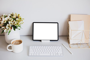 Digital tablet mockup with pen, keyboard, cup of coffee, paper notebooks, flowe