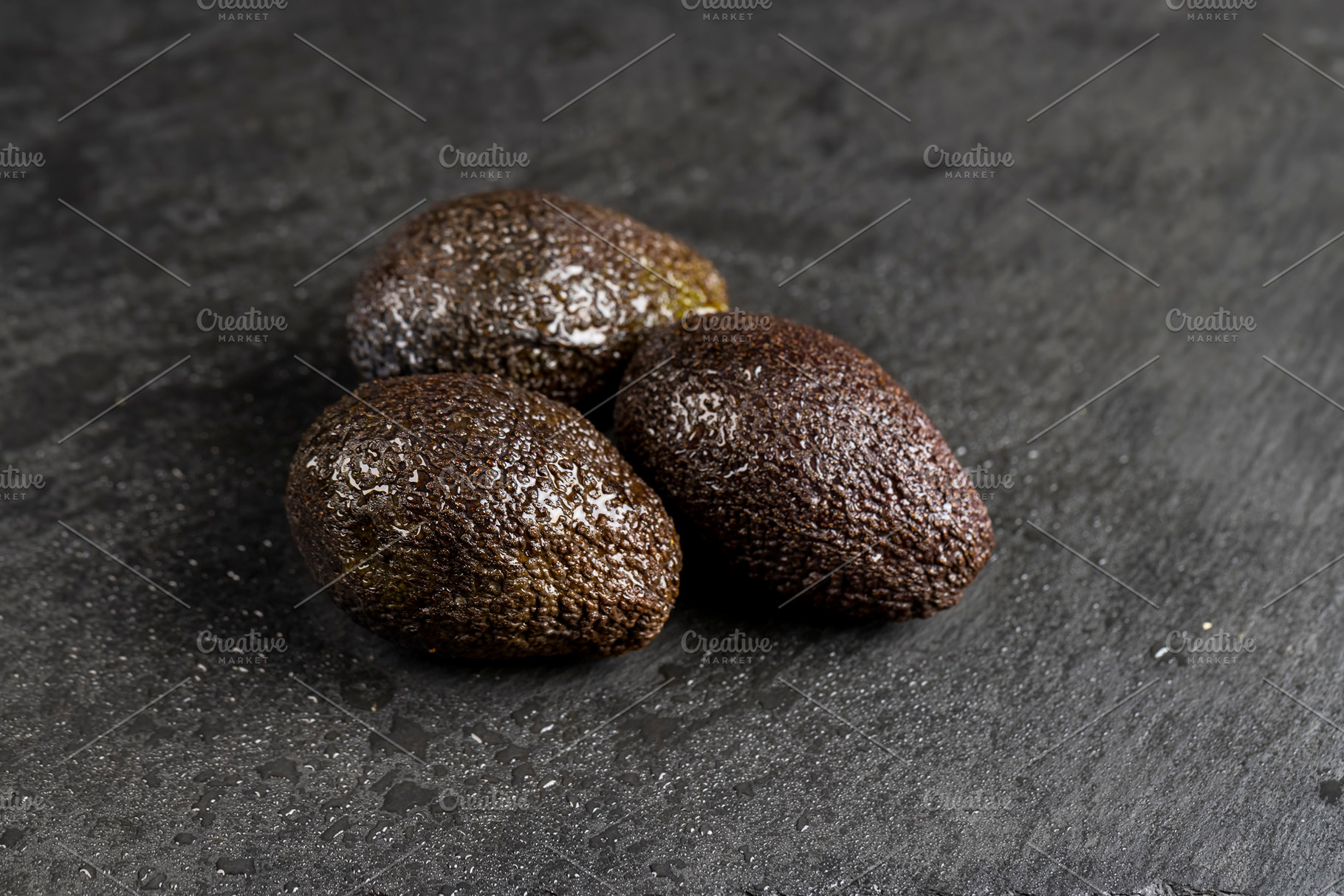 wet whole black avocado fruits of small size on a black slate, a Photo by rsoollAI