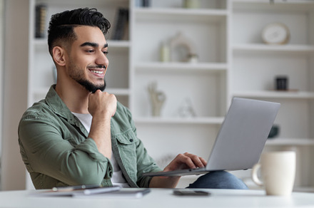 Portrait Of Smiling Handsome Young Arab Man On Laptop At Home Office, a Photo by Prostock-Studio
