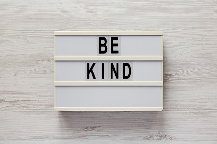 'Be kind' on a lightbox on a white wooden surface, top view. Fla, a Business Photo by LiudmylaChuhunova