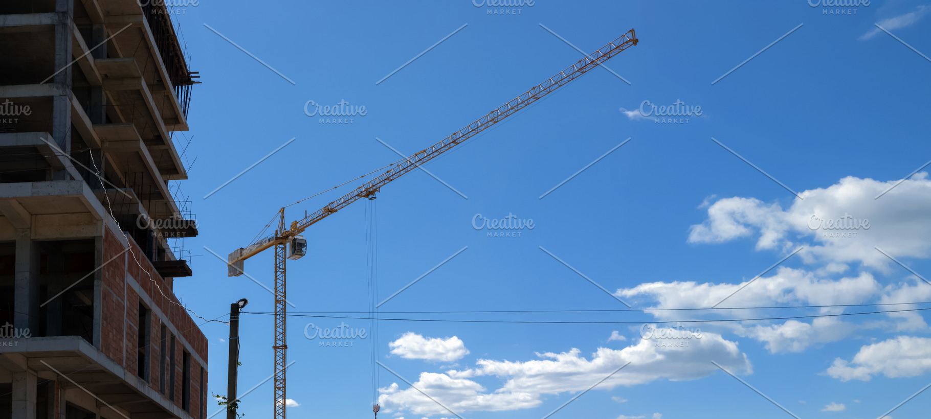 Wide view of a yellow tower crane next to a concrete building un, an Industrial Photo by Ales Munt