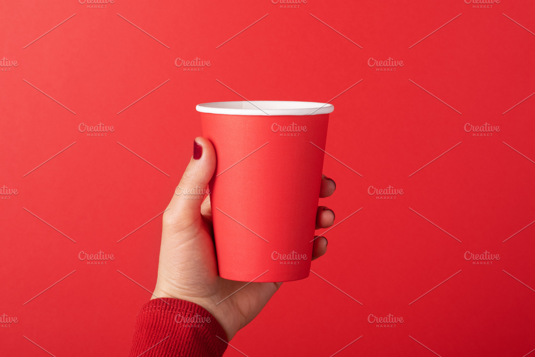 Female hand holding a red paper cup against a matching red backg, a Food & Drink Photo by Ales Munt
