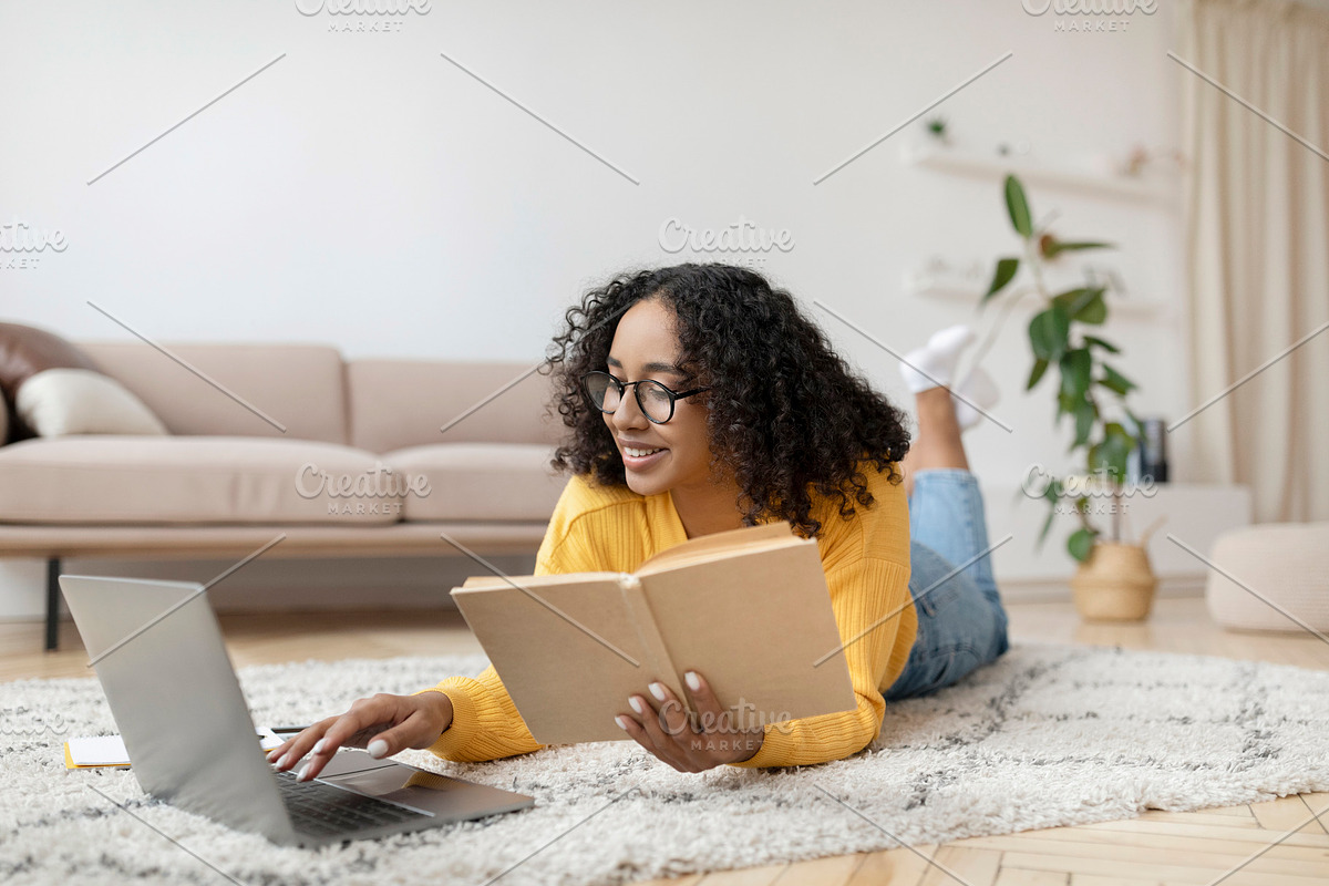 Young black woman reading book near laptop, getting ready for exam or working o, a Photo by Prostock-Studio (Photo 2 of 2)