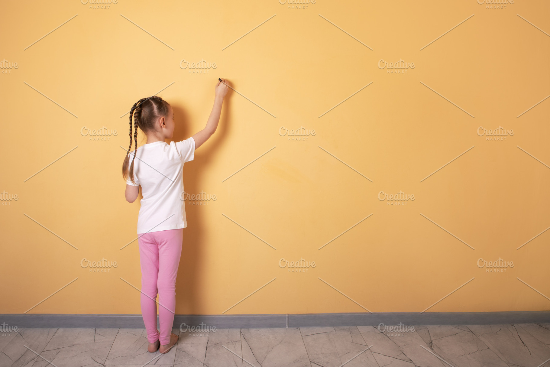 Young girl with braids draws on a blank yellow wall, viewed from, a Person Photo by Ales Munt