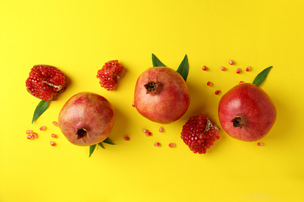 Ripe pomegranate, leaves and seeds on yellow background, a Food & Drink Photo by AtlasStudio PRO