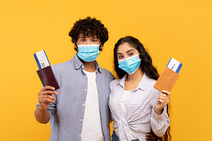 Young indian couple wearing protective face masks, holding passports and flight, a Person Photo by Prostock-Studio
